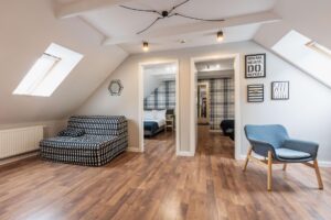 wejście do dwóch pokoi, biało-czarna kanapa po lewej stronie, szare krzesło po prawej